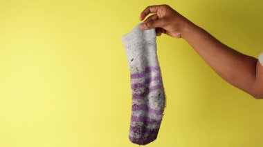 Ellerinde yıpranmış bir çorap var, sarı lekeler ve solmuş renkler var..