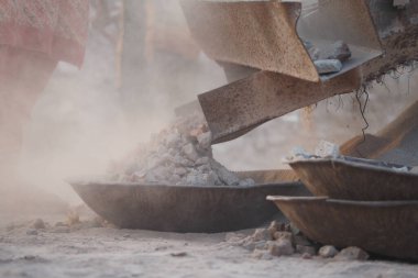 İşçiler tozlu bir taş ocağında çakıl çıkarmak ve işlemek için makineler kullanırlar..