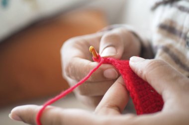 İnsan, kırmızı bir örgü örer. Kapalı alanda kanca ve iplik kullanır..