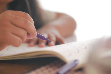 Bir çocuk evdeki bir defterde sanat yaratmak için mor bir kalem kullanır..
