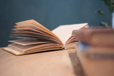 Açık bir kitap, bulanık ciltlerle çevrili ahşap bir masanın üzerinde duruyor..