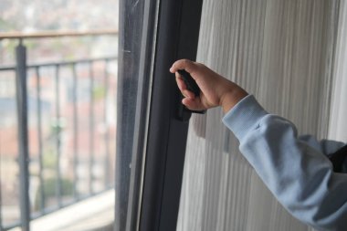 Bir çocuk temiz hava ve güneş ışığı için pencere koluna uzanır..