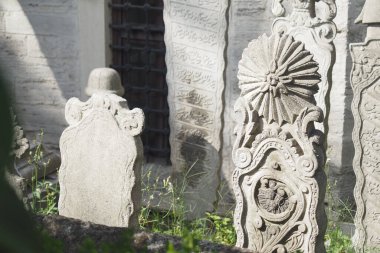 Ayrıntılı mezar taşları dingin bir mezarlıkta yeşilliklerin arasına yerleştirilmiştir..