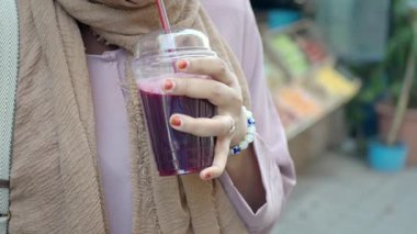 Bir kadın canlı bir taze ürün pazarında renkli bir içecekten hoşlanır..