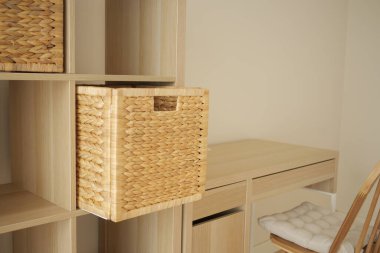 Bir masanın yanındaki hafif ahşap rafta dokuma bir sepet duruyor..