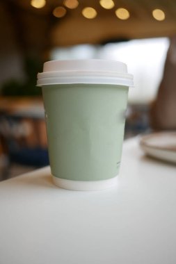 Parlak bir kafedeki masada basit bir bardak ılık içecek duruyor..