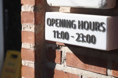 Tuğla duvarda saat 11 'den 23' e kadar açık olduğunu gösteren bir tabela var..