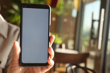 Gündüz vakti bir kafede elinde boş bir ekranla akıllı telefon tutan biri..
