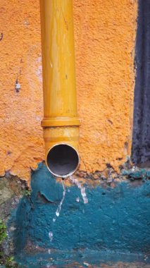 Su sürekli sarı bir borudan renkli bir duvara damlıyor..