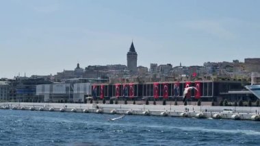 Sersemletici ufuk çizgisi Galata Kulesi ve hareketli bayraklarla dolu rıhtım.