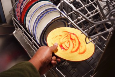 Bir el bulaşık makinesinden sosla kaplı sarı bir tabağa uzanır..