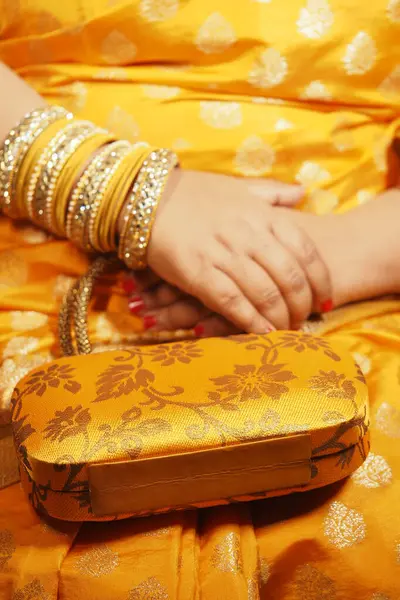 Bileziklerle süslenmiş eller bir kutlamada altın bir cüzdanın üzerinde dinleniyor..
