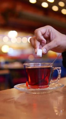 Bir kafe masasında otururken birisi bir fincan sıcak çaya şeker karıştırır..