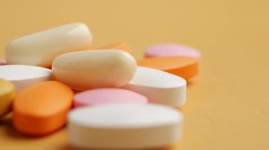 Çeşitli tabletler ve kapsüller parlak sarı bir yüzeye dizilmiştir..