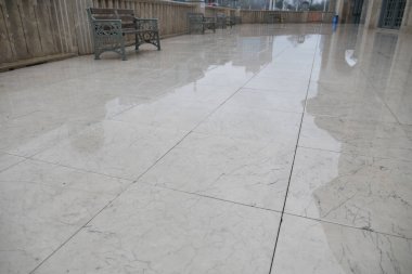 Avluda, yeni yağan yağmurdan yansıyan su birikintilerini yansıtan parlak mermer bulunuyor.