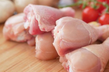 Çiğ tavuk budu, yakınlarda sebzelerle birlikte ahşap bir tahtaya dizilir..