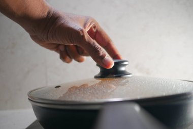 Parlak mutfak ortamında kaynayan tencerenin kapağına uzanır..