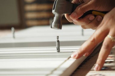 Bir insan, tahta bir yüzeye çivi çakmak için çekiç kullanıyor..