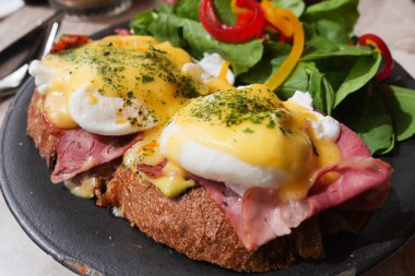 Taze hazırlanmış yumurtalı Benedict salatalı kızarmış ekmeğin üzerinde oturur..