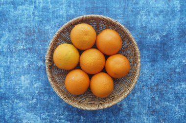 Mavi kumaş üzerinde düzenlenmiş canlı portakallarla dolu bir sepet..
