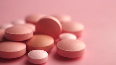 Değişen boyutlarda yuvarlak tabletler yumuşak pembe bir yüzey üzerinde dinleniyor..