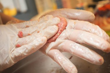 Eldivendeki eller çiğ eti köfteye dönüştürüyor. Bu da yemek hazırlığını gösteriyor..