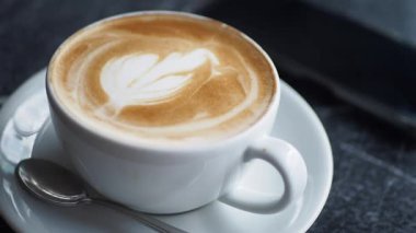 Karmaşık sanatlarla hazırlanmış güzel bir latte telefonun yanındaki masada oturur..