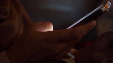 Gece loş ışıkta akıllı telefon ekranı ile etkileşime giren kişi.