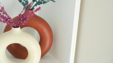 Parlak renkli vazolarda kurumuş çiçekler modern bir rafta sergilenir..
