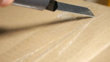 Bir insan kahverengi bir karton kutunun üzerindeki bandı dikkatlice keser..