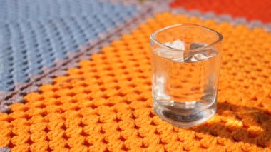 Suyla dolu bir bardak, gün ışığında canlı bir battaniyenin üzerinde oturur..