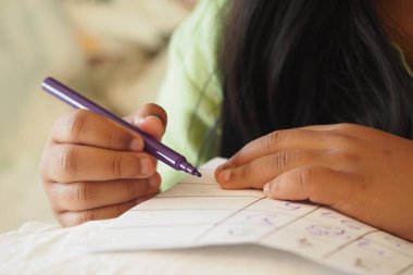 Bir çocuk yumuşak bir yüzeye mor bir kalemle notlar yazar..