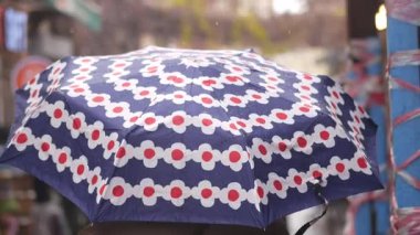 Şehirde yağmur yağarken bir kişi canlı bir şemsiye altında yürür..