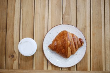 Kruvasan, bir tabağın üzerine, ahşap bir masada kahve fincanının yanına..