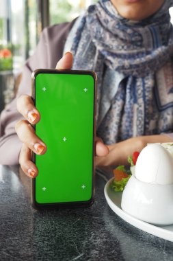 Kafe masasında oturan biri, boş ekranlı bir akıllı telefonu sergiliyor..