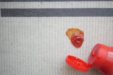 Parlak kırmızı ketçap lekesi çizgili bir halıyı işaret ediyor..