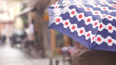 Yağmurlu bir şehir caddesinde elinde canlı bir şemsiyeyle yürüyen bir insan..