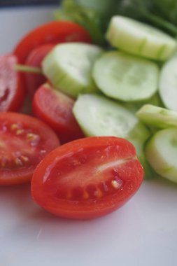 Sulu domatesler ve çıtır salatalıklar beyaz bir tabakta sıralanır..