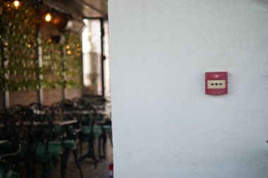 Yeşil sandalyeli kalabalık bir yemek alanında duvara asılmış klasik bir yangın alarmı..