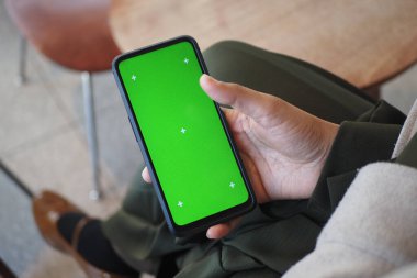 Bireysel olarak otururken yeşil ekran gösteren bir akıllı telefon sergiliyor.