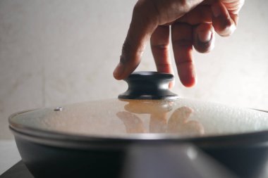 Bir el yemek pişirmek için ocağın tepesine kapak koyuyor..