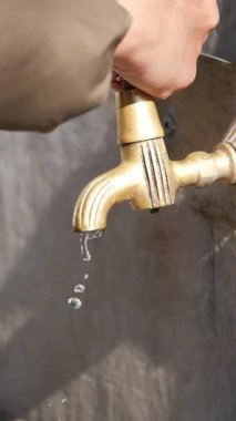 Bir el pirinçten musluğu döndürür ve kırsal bölgede suyun yavaşça damlamasına neden olur..