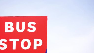 Açık mavi bir gökyüzünün altında, toplu taşıma araçlarını gösteren bir otobüs durağı tabelası..