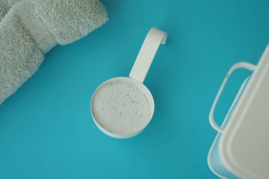 Beyaz bir bardak çamaşır deterjanı havluların yanında mavidir..