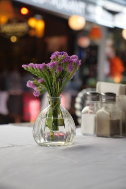 Canlandırıcı çiçeklerle dolu cam bir vazo bir kafe masasında duruyor..