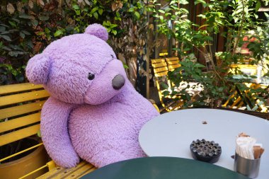 Mor bir ayı yemyeşil bir ortamda bir kafe masasında dinlenir..