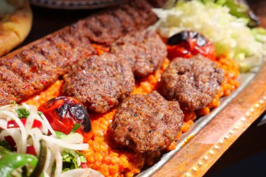 Baharatlı pirinç ve taze yeşilliklerle birlikte lezzetli kebaplar servis edilir..