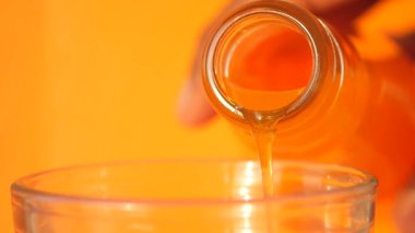 Sıvı bir şişeden bardağa akıyor, canlı turuncu bir arkaplan vurguluyor..