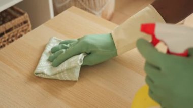 Kişi ahşap bir yüzeyi bir bez ve sprey temizleyiciyle temizler..