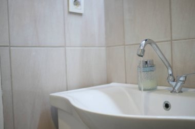 Pürüzsüz bir musluktan temiz bir banyoda beyaz bir lavaboya su akıyor..